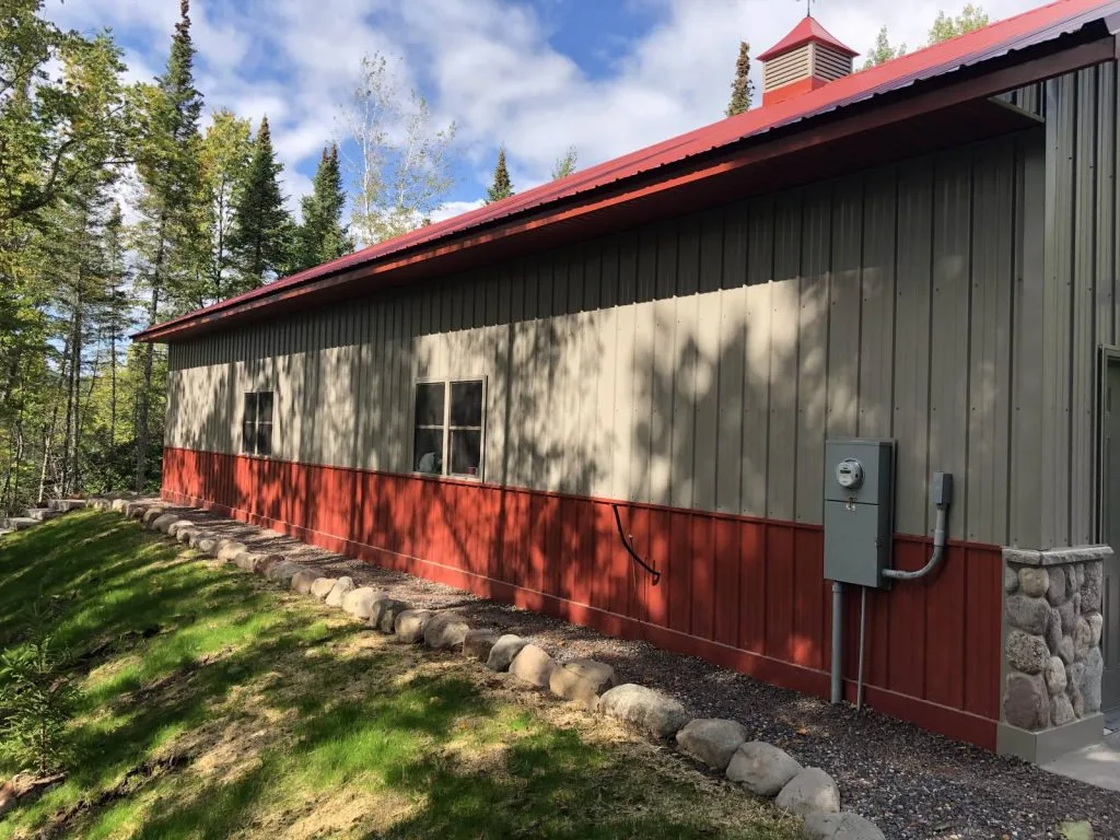 Side of a Keenan shop building with metal siding, red trim and a stone base
